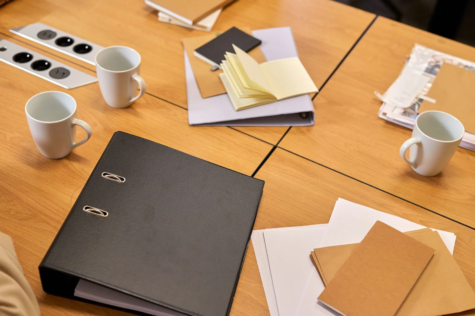 A tidy office desk with ring binders, loose papers and two coffee mugs arranged on it.