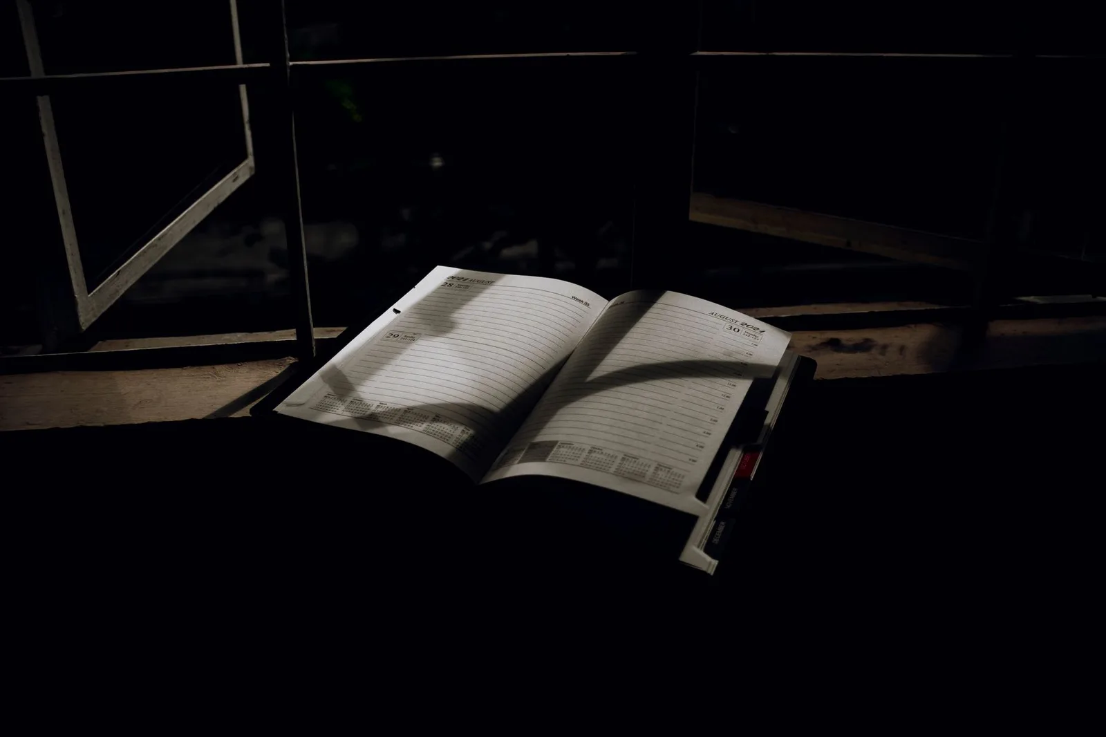 An open paper planner lying on a window sill in low evening light, its monthly pages blank.