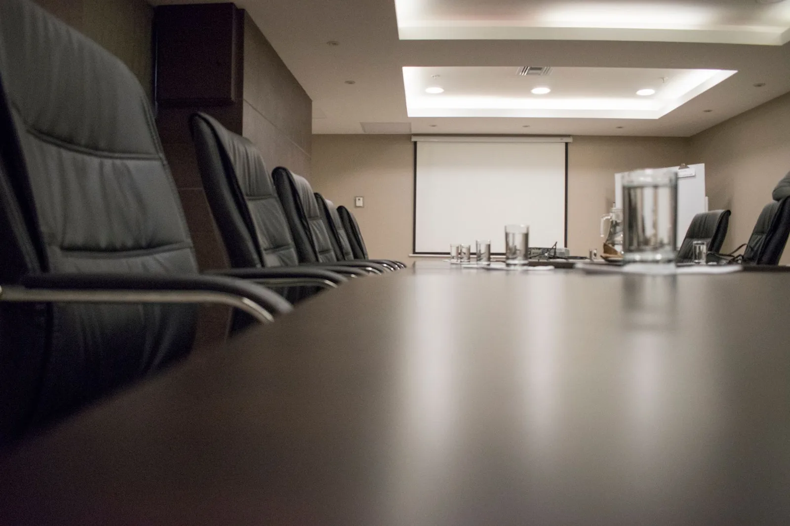 An empty meeting room with black chairs set around a long table, a projector and a pair of glasses on the table.