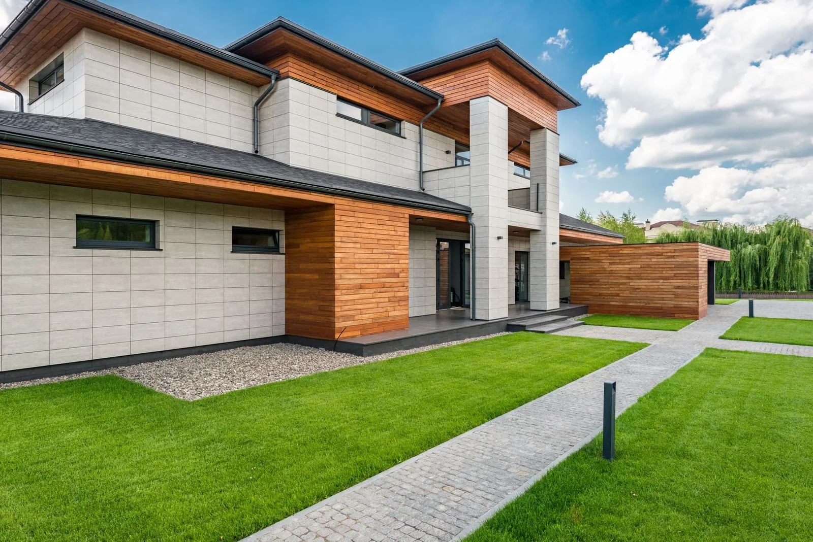 A single storey contemporary house with a green lawn and paved paths on a sunny day.
