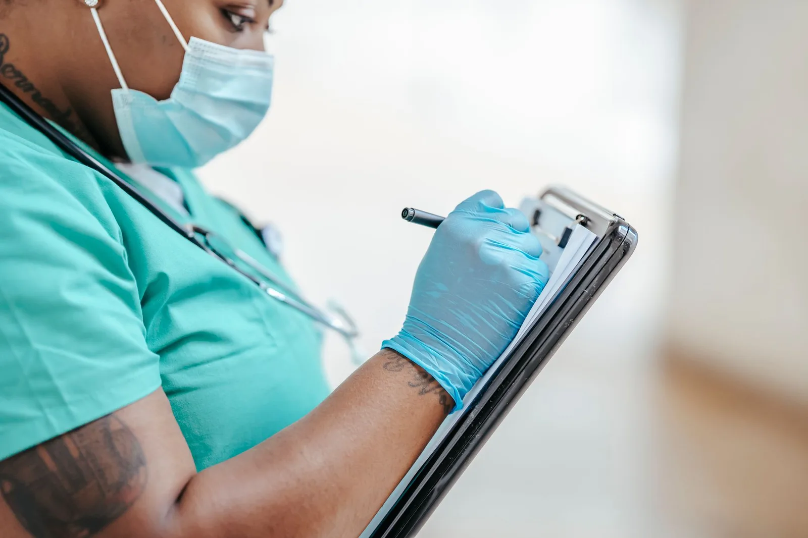 A health worker in uniform, seen from the side, writing notes on a paper form held on a clipboard.